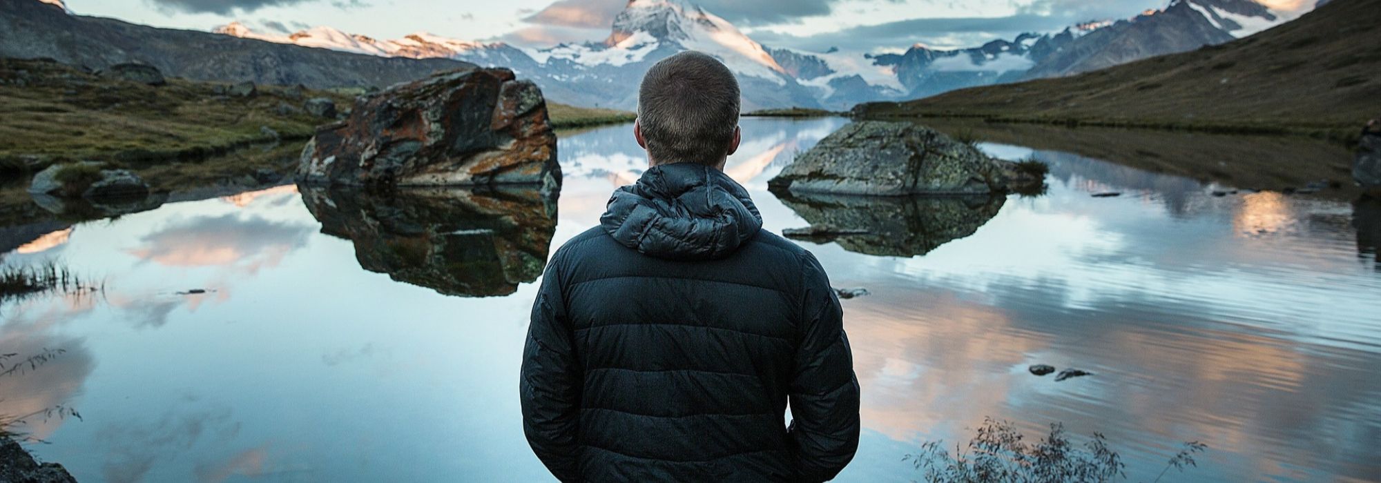 Veste chauffante noire portée par un homme face à un lac de montagne en hiver